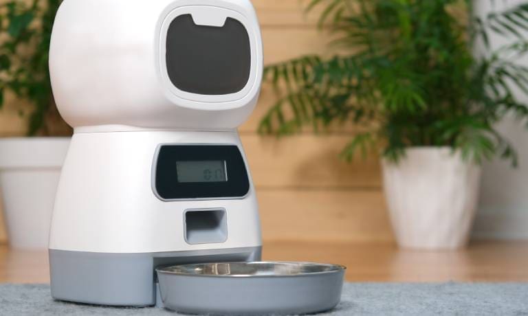 How Smart Devices Can Help You Be a Better Dog Owner 1 An unmarked white automatic pet food dispenser with a gray bowl sitting on the floor of a home.