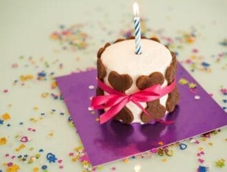 A birthday cake with an ignited candle sitting on top. There are brown dog bones surrounding the outer edge of the cake.