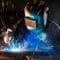 A worker performing argon welding on metal with a torch as bright sparks flare from the point of contact.