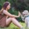 A dog owner sitting on the grass with a puppy and encouraging it to lift its paw and hold it against their hand.
